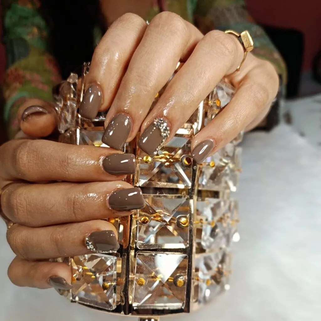 Glossy brown nails with elegant stone detailing in Thrissur.